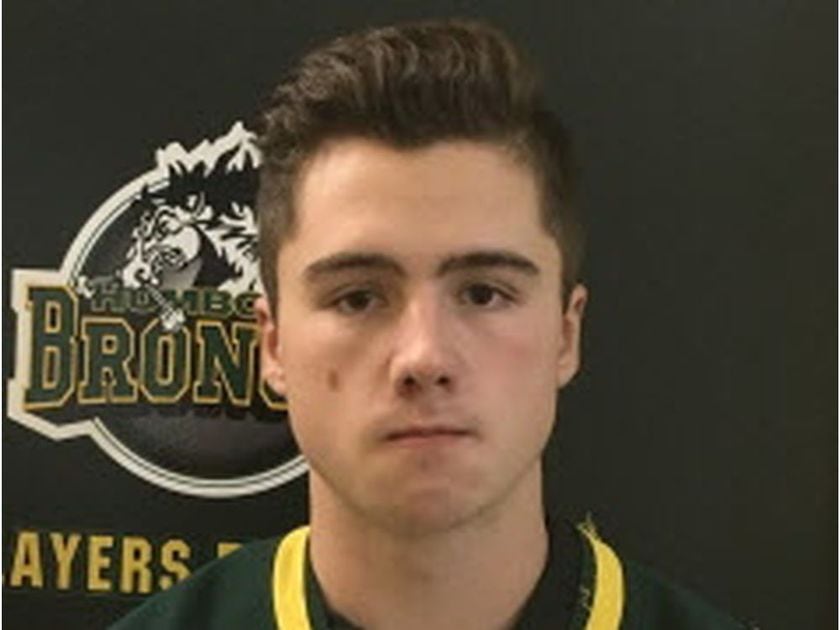 A young man posing in front of a Humboldt Broncos logo.