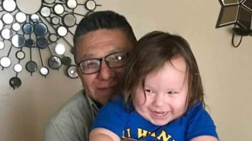 A smiling man hugs and holds a laughing toddler.