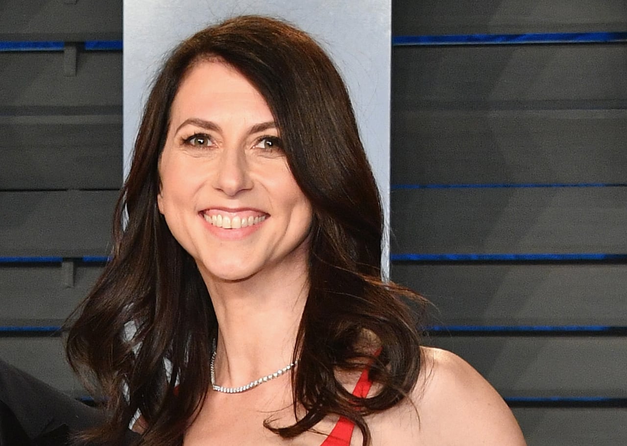 A smiling woman with long brown hair and a diamond necklace